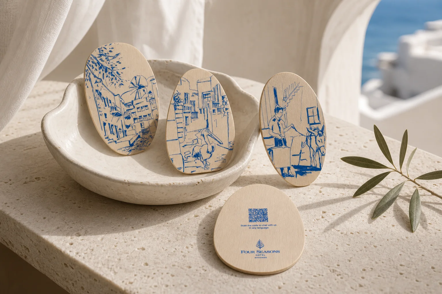 Four Seasons Mykonos wooden key cards displayed in a ceramic bowl on a travertine ledge with an olive branch and the Aegean Sea in the background