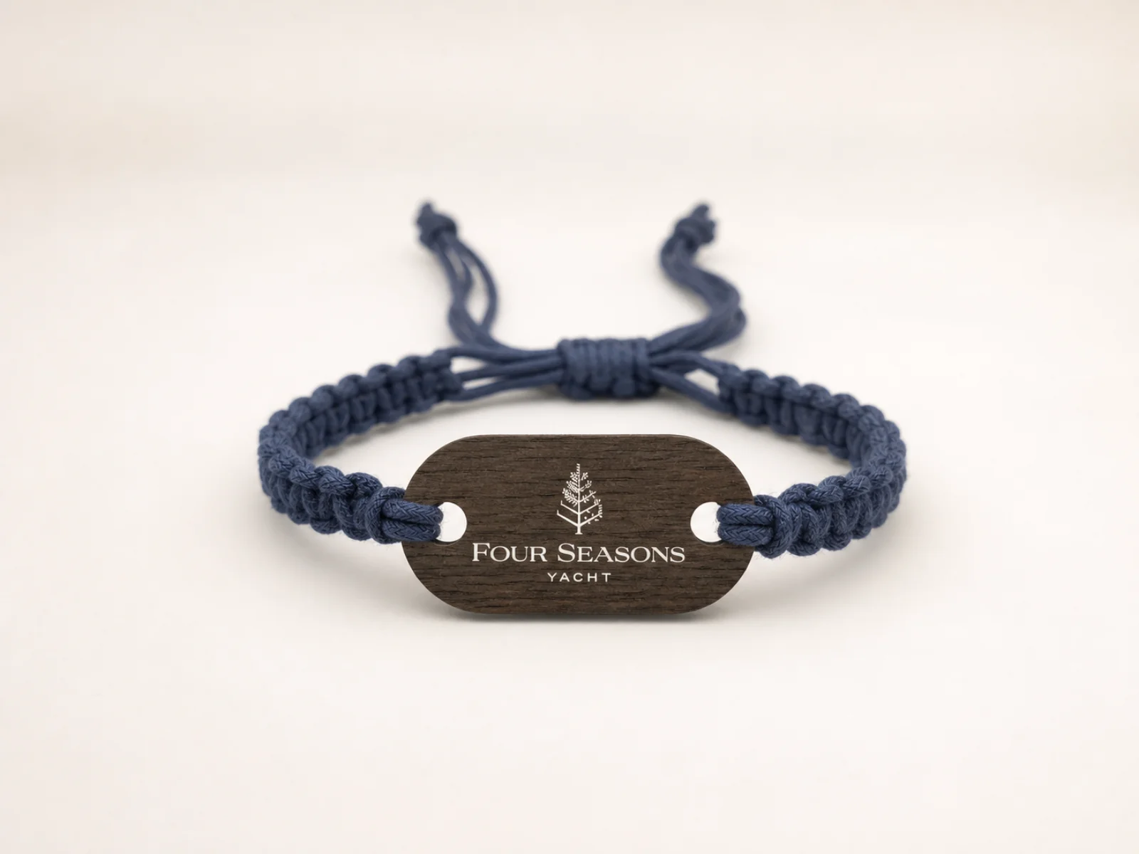 Four Seasons Yacht wooden RFID wristband studio view — dark walnut plaque printed with the Four Seasons tree logo, mounted on an adjustable navy macramé cord