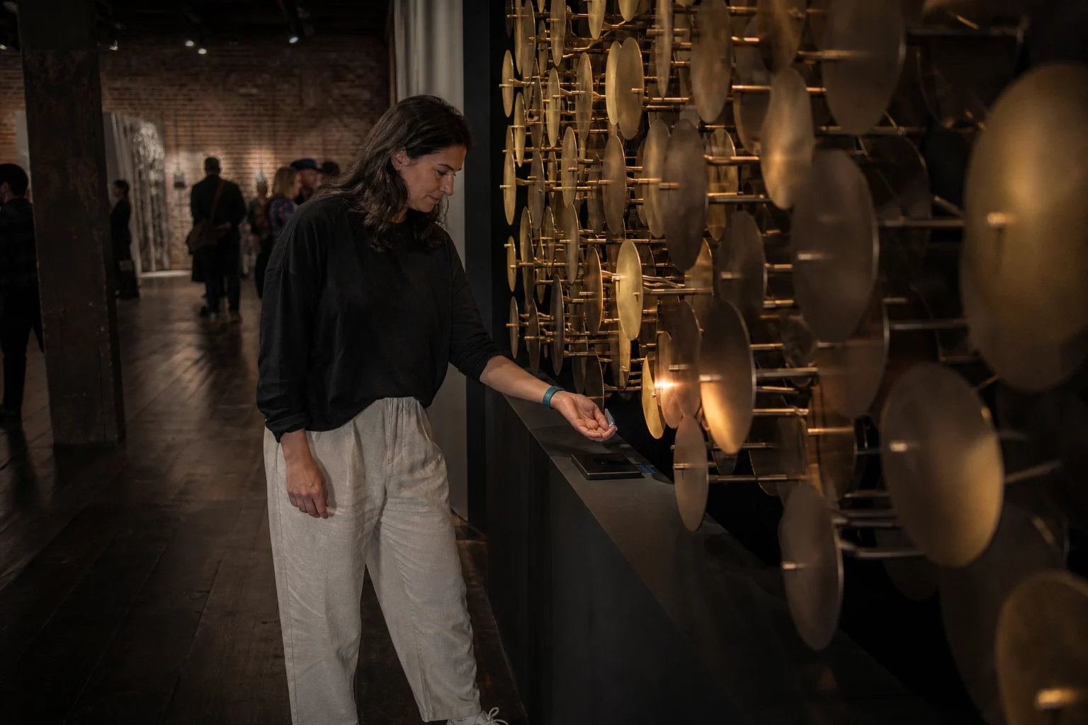 Arts-event guest using a teal silicone RFID wristband at a kinetic brass installation